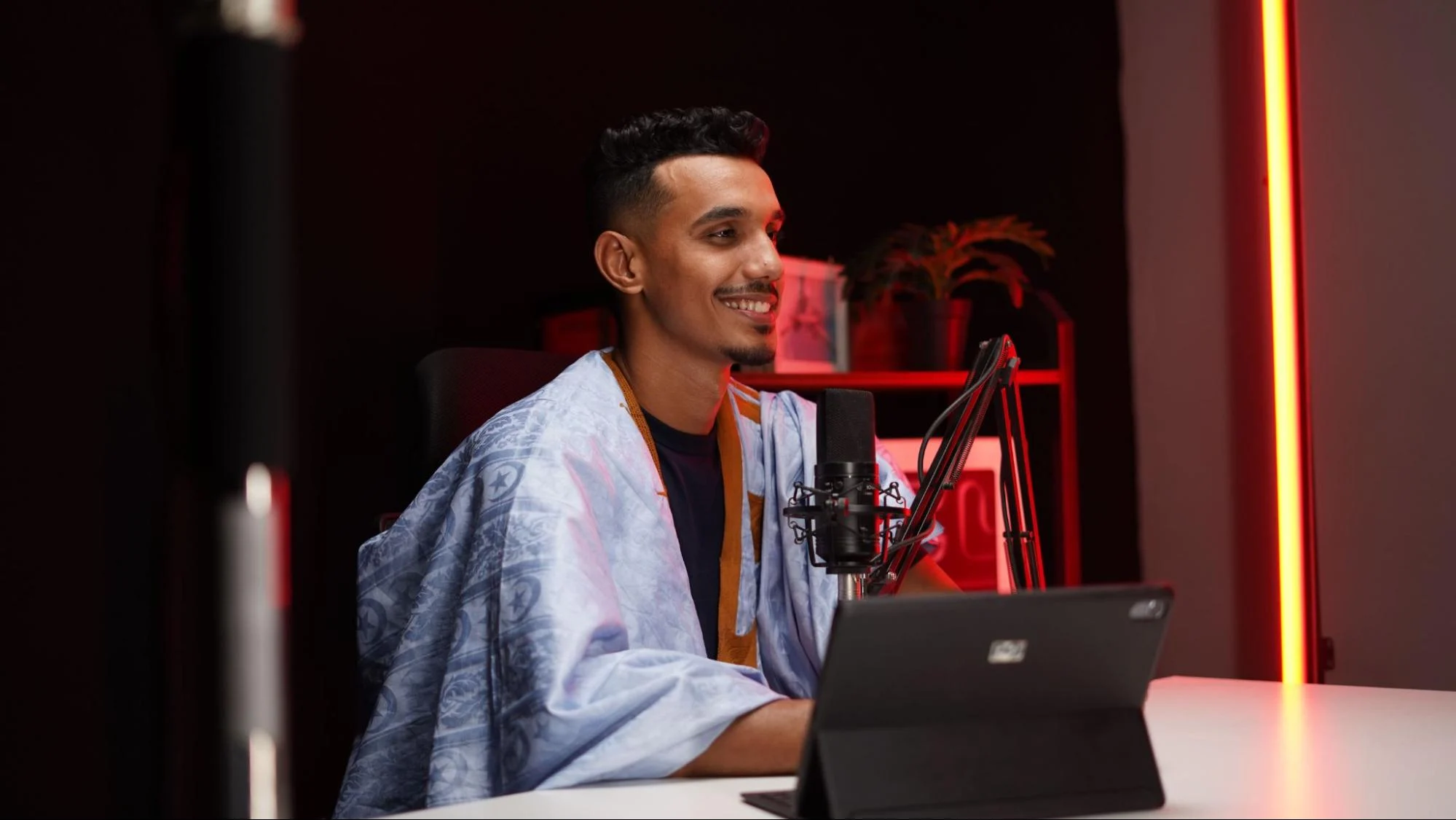 Person recording video content at a desk with a microphone and laptop in a studio setup